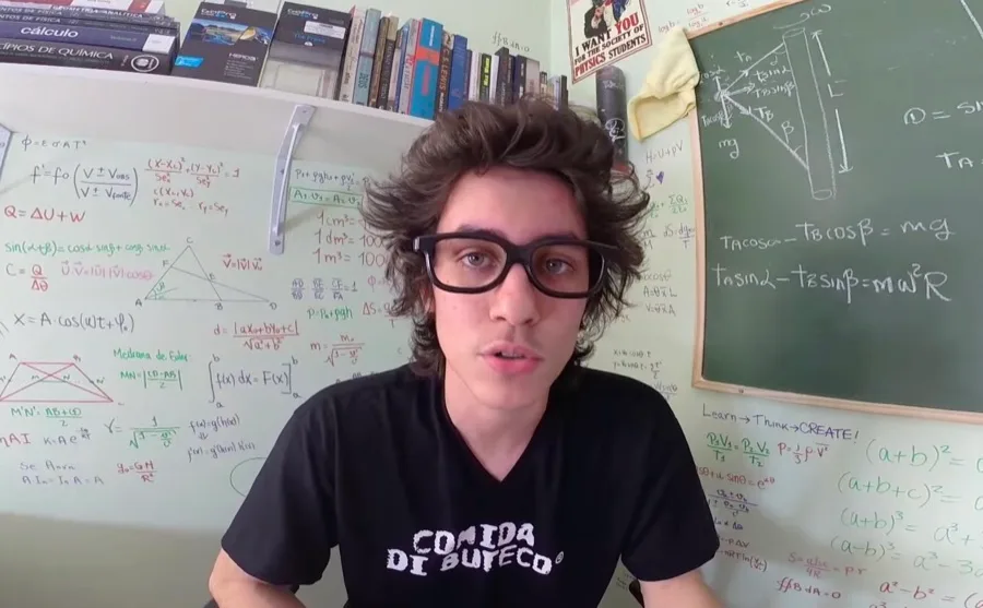 Felipe aos 17, de óculos, no quarto com a parede cheia de fórmulas e um quadro-negro