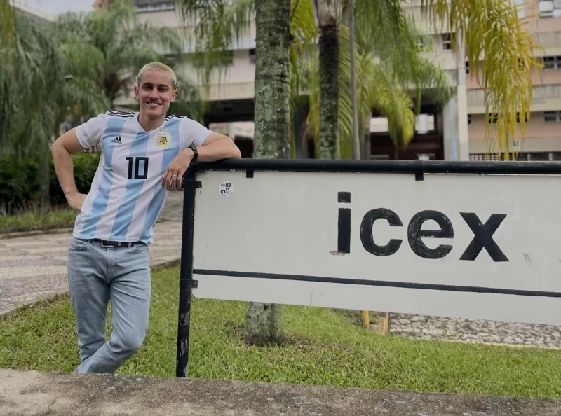 Felipe encostado na placa do ICEx, na UFMG