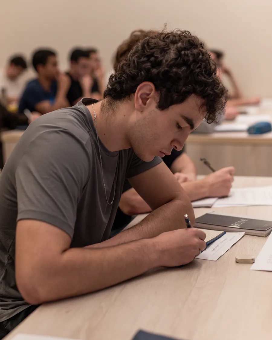 Aluno resolvendo a lista na carteira durante a aula