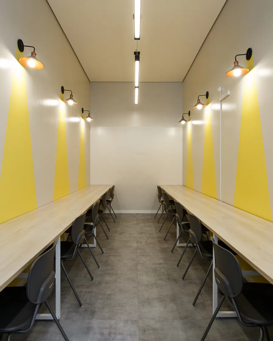 Sala de estudo com bancadas de madeira nas duas paredes e luminárias sobre faixas amarelas