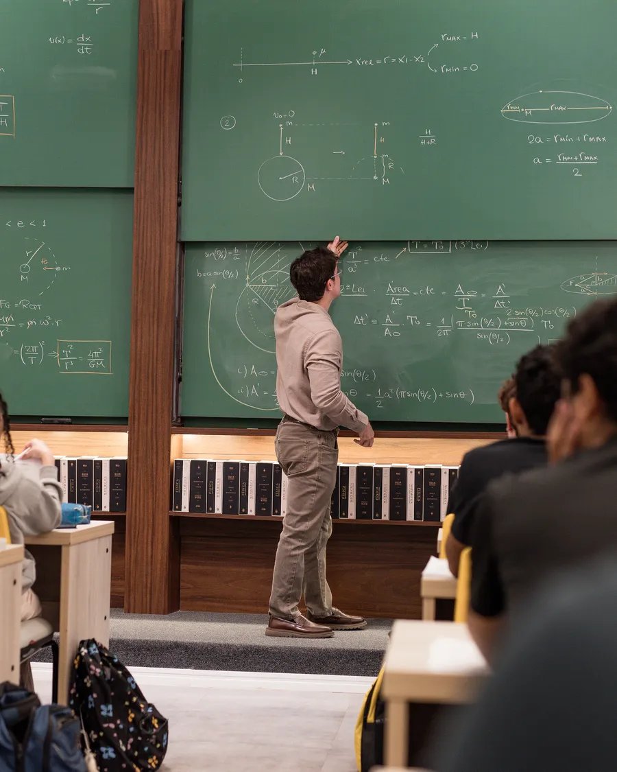 Professor no quadro verde durante a aula de gravitação, com a turma acompanhando