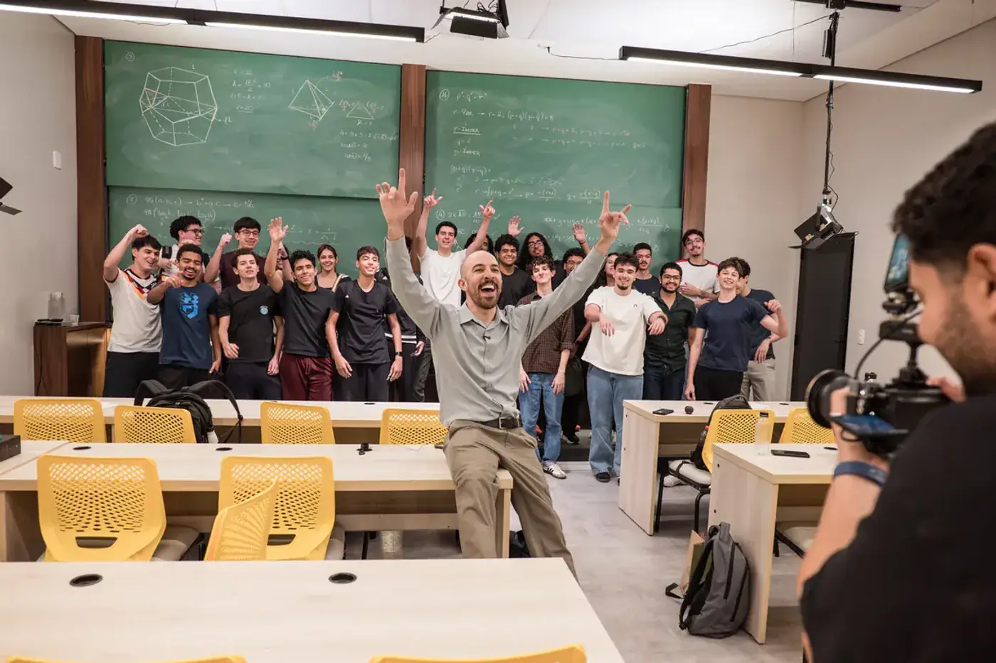 A turma comemorando de braços erguidos enquanto a câmera grava a aula